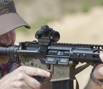 A shooter aiming down the sights of an advanced rifle equipped with a red dot scope 
